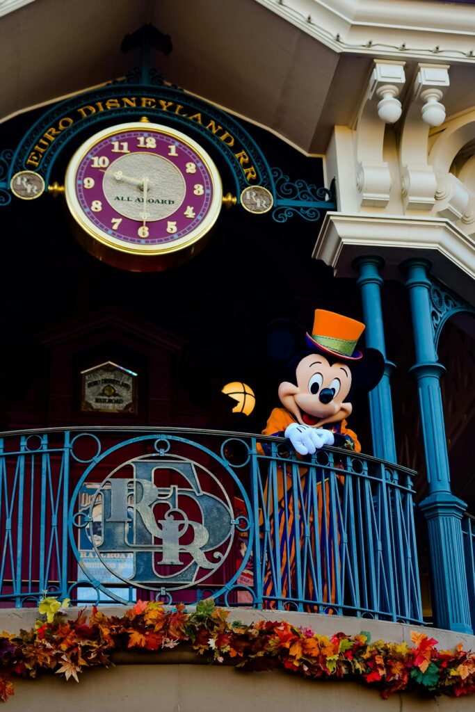 Mickey Mouse dressed for fall at Disneyland Paris, with autumn decor on a balcony.